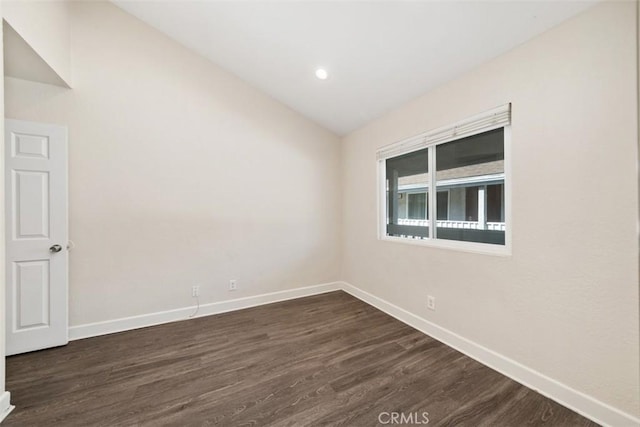 spare room featuring dark wood-style floors, vaulted ceiling, and baseboards