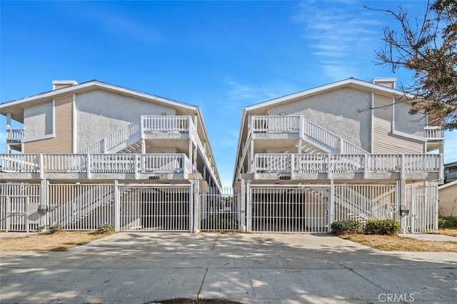 view of front of property featuring a chimney, stucco siding, stairway, a gate, and fence