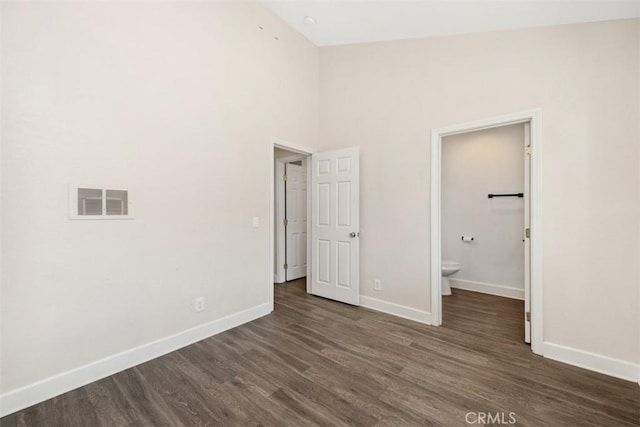 unfurnished bedroom featuring visible vents, connected bathroom, baseboards, and dark wood-type flooring