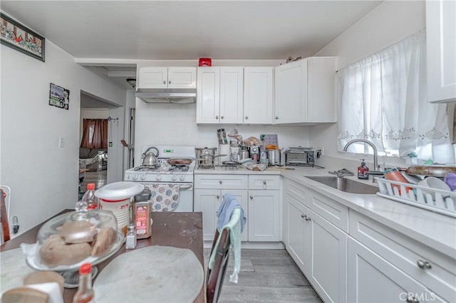 kitchen with white range with gas cooktop, sink, white cabinets, and light wood-type flooring