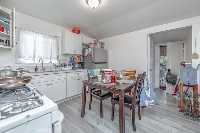 kitchen with stainless steel fridge, white cabinetry, vaulted ceiling, and light hardwood / wood-style floors