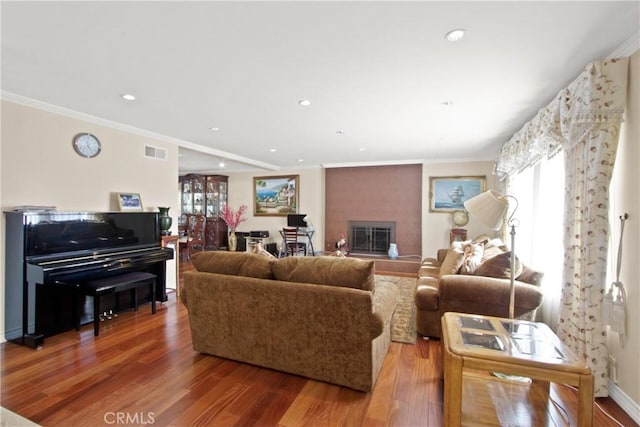 living room with a large fireplace, ornamental molding, and hardwood / wood-style flooring