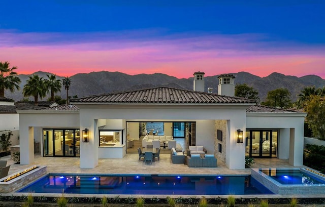 back house at dusk featuring outdoor lounge area, a mountain view, a pool with hot tub, and a patio area