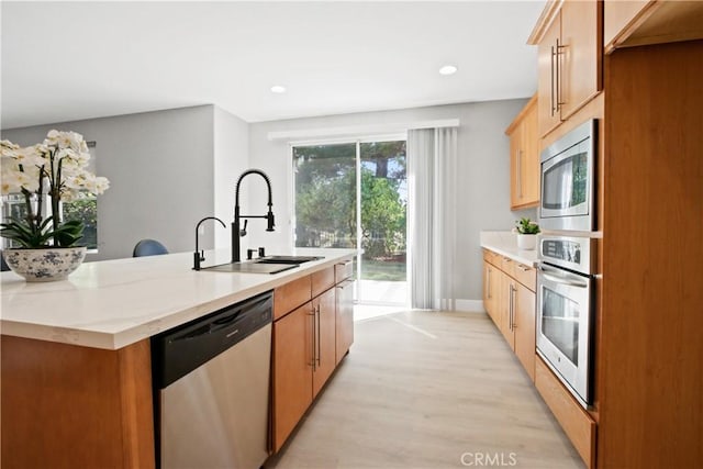 kitchen with sink, an island with sink, stainless steel appliances, and light wood-type flooring