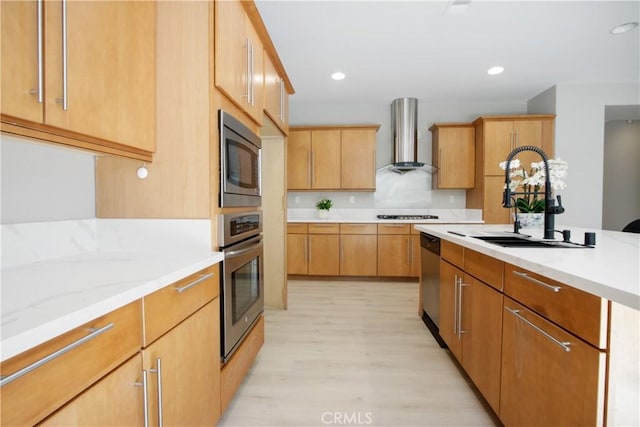 kitchen featuring light wood-type flooring, light stone counters, wall chimney exhaust hood, stainless steel appliances, and sink