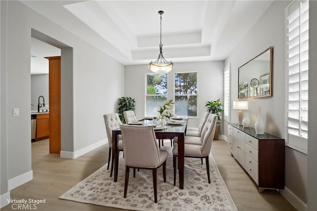 dining room with light wood-type flooring, a tray ceiling, and sink