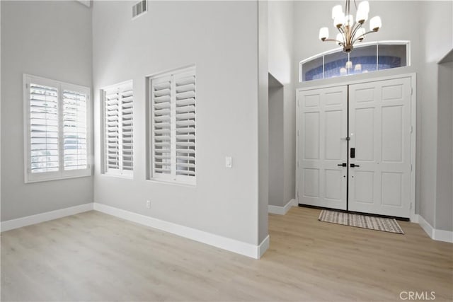 foyer with light hardwood / wood-style flooring, a high ceiling, and an inviting chandelier