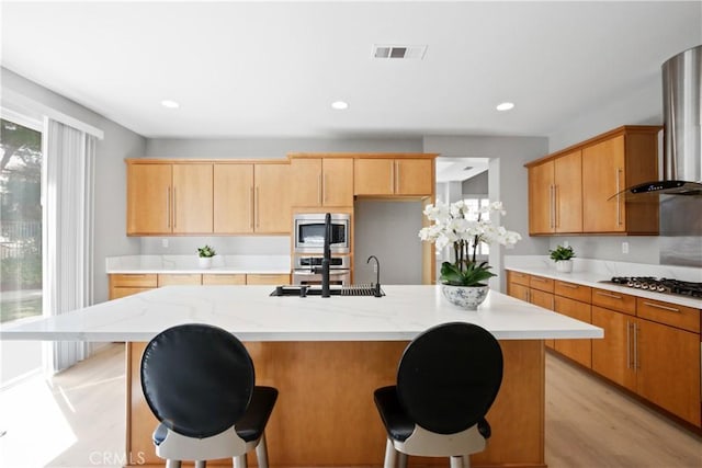 kitchen with a breakfast bar, stainless steel appliances, light hardwood / wood-style floors, and an island with sink