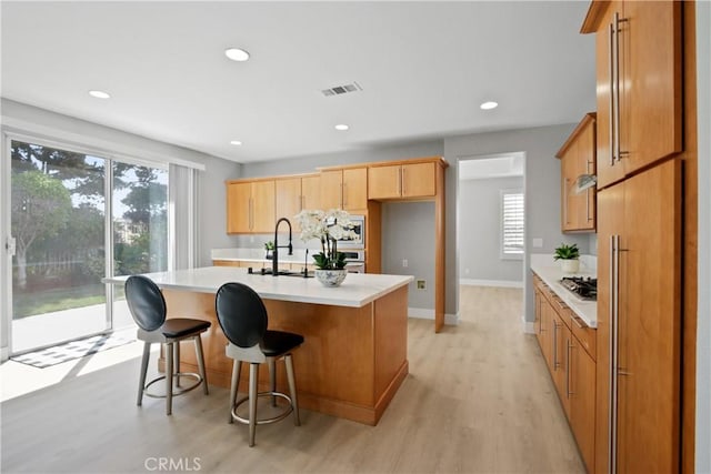 kitchen featuring a breakfast bar, a center island with sink, a healthy amount of sunlight, and light hardwood / wood-style floors