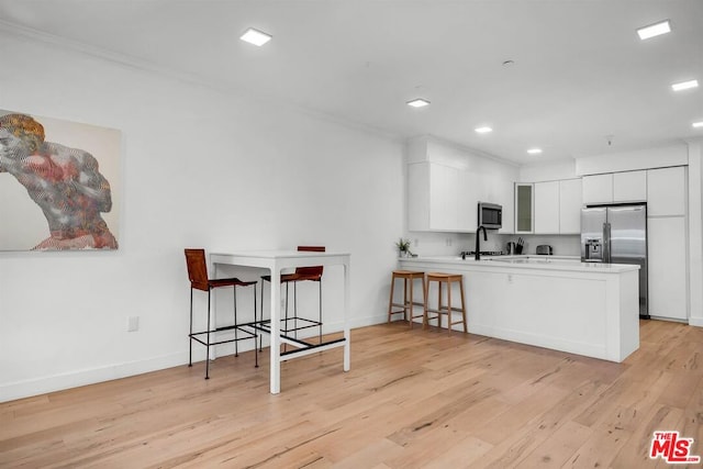 kitchen featuring kitchen peninsula, appliances with stainless steel finishes, a kitchen breakfast bar, light hardwood / wood-style floors, and white cabinetry