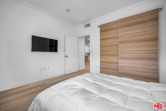 bedroom featuring hardwood / wood-style floors, ornamental molding, and a closet