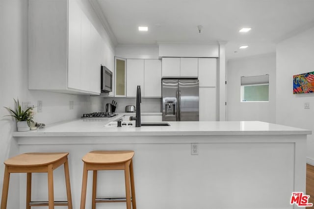 kitchen with a kitchen breakfast bar, sink, kitchen peninsula, appliances with stainless steel finishes, and white cabinetry