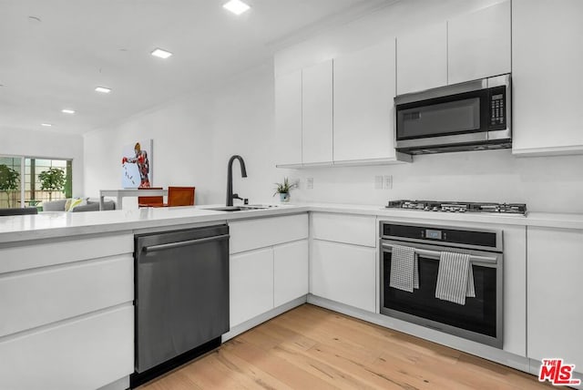 kitchen with white cabinets, appliances with stainless steel finishes, light hardwood / wood-style flooring, and sink