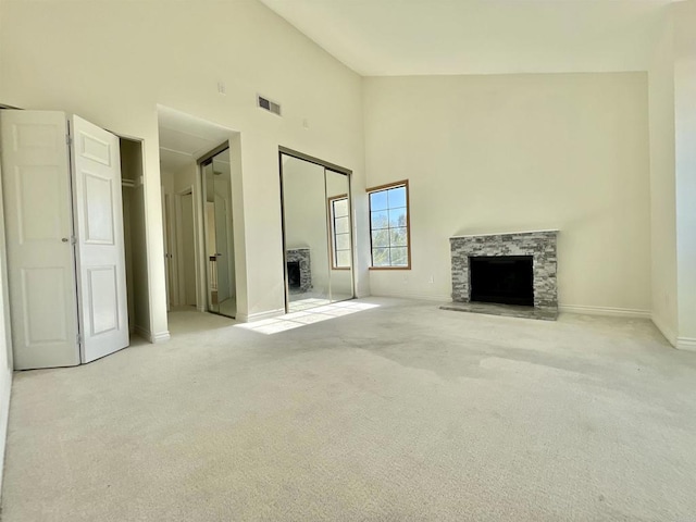 unfurnished living room featuring light colored carpet, a towering ceiling, and a fireplace