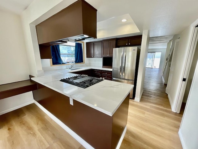 kitchen featuring sink, light hardwood / wood-style flooring, dark brown cabinets, kitchen peninsula, and stainless steel appliances