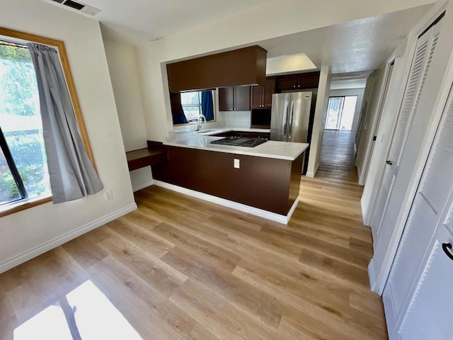 kitchen with kitchen peninsula, stainless steel fridge, dark brown cabinetry, sink, and light hardwood / wood-style flooring