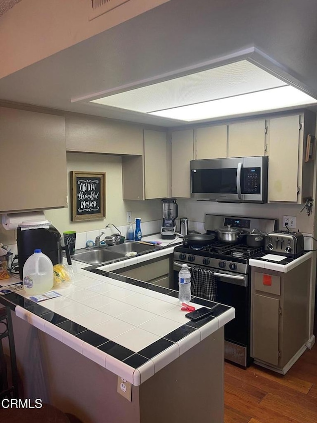 kitchen with stainless steel appliances, dark wood-type flooring, a peninsula, a sink, and tile counters