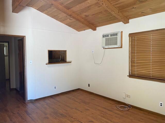 empty room featuring dark hardwood / wood-style flooring, lofted ceiling with beams, a wall mounted AC, and wooden ceiling