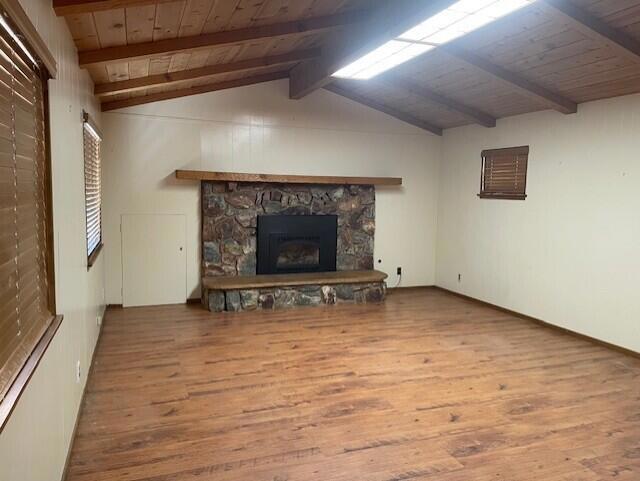 unfurnished living room with hardwood / wood-style floors, lofted ceiling with beams, a stone fireplace, and wood ceiling