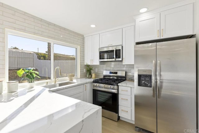 kitchen featuring white cabinetry, stainless steel appliances, backsplash, light stone counters, and sink