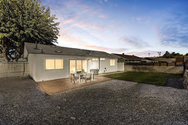 back house at dusk featuring a patio area and a yard