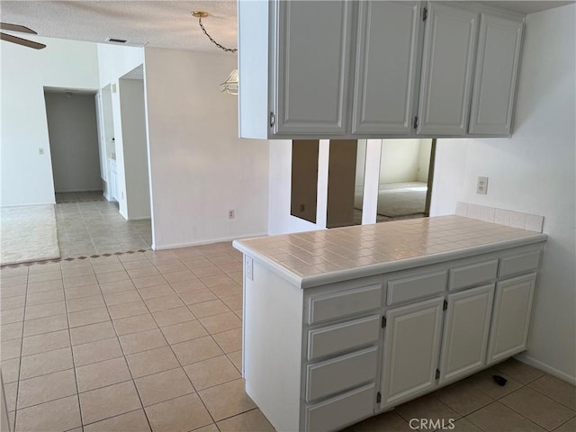 kitchen featuring tile counters, kitchen peninsula, a textured ceiling, light tile patterned flooring, and ceiling fan with notable chandelier