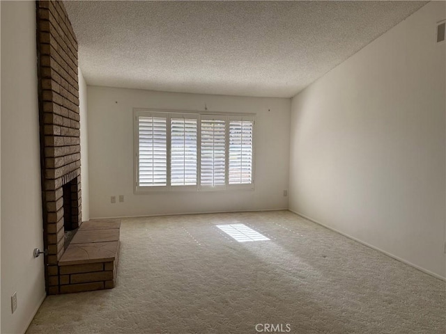 carpeted spare room featuring a textured ceiling and a brick fireplace