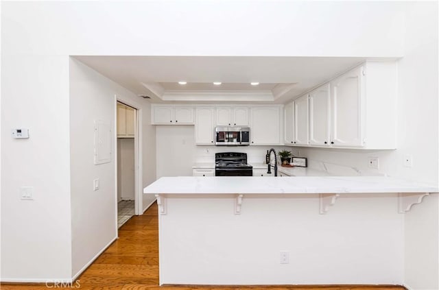 kitchen featuring kitchen peninsula, a tray ceiling, a kitchen breakfast bar, and black electric range oven