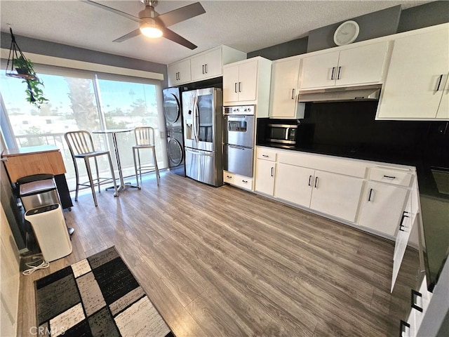 kitchen featuring ceiling fan, stainless steel appliances, stacked washer and dryer, light hardwood / wood-style floors, and white cabinets