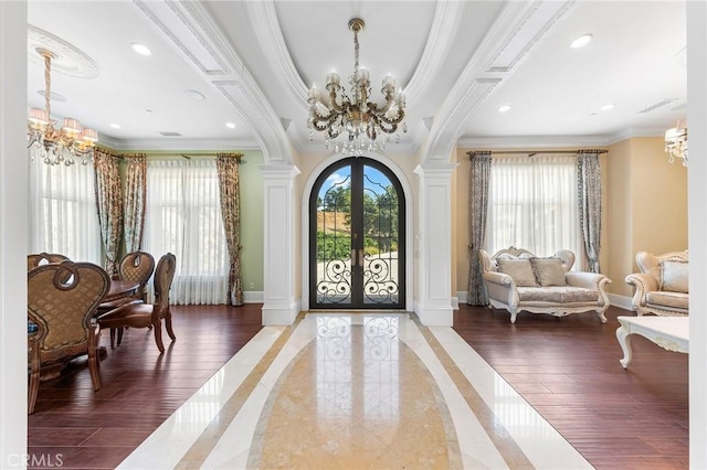 entrance foyer featuring french doors, a notable chandelier, decorative columns, crown molding, and hardwood / wood-style floors