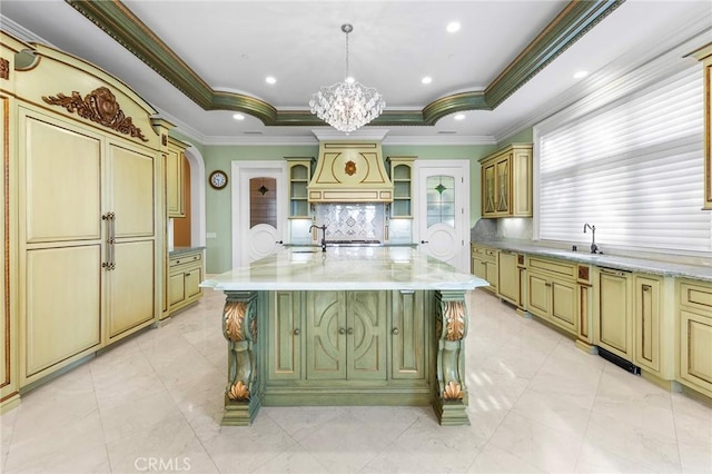 kitchen with pendant lighting, a center island with sink, a raised ceiling, crown molding, and decorative backsplash