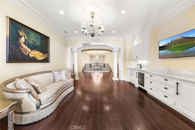 corridor featuring an inviting chandelier, crown molding, dark hardwood / wood-style floors, beverage cooler, and decorative columns