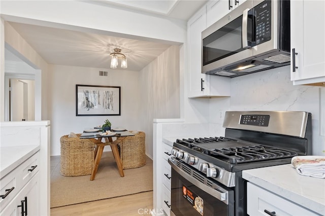 81 Smokestone Unit 12, Irvine, CA 92614 - kitchen with appliances with stainless steel finishes, white cabinetry, light wood finished floors, and light stone counters