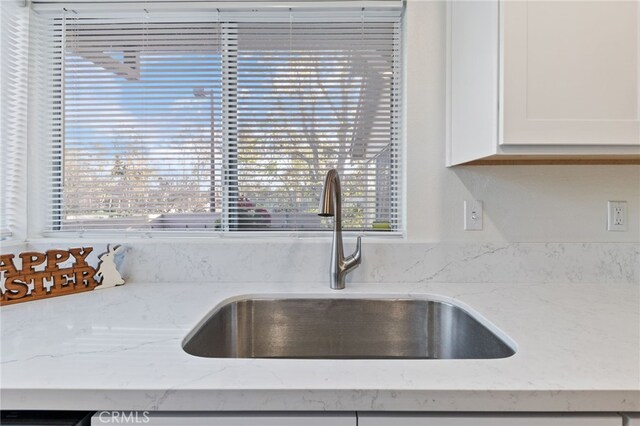 interior details featuring a sink, white cabinets, and light stone countertops