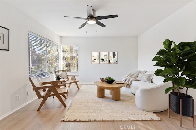 living area with baseboards, ceiling fan, and light wood-style flooring