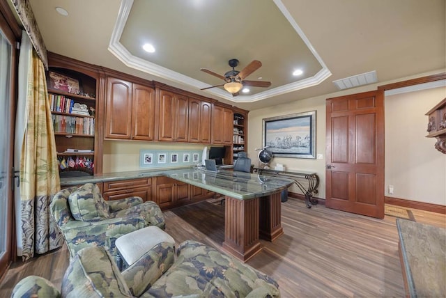 office space with ornamental molding, a tray ceiling, ceiling fan, built in desk, and hardwood / wood-style floors