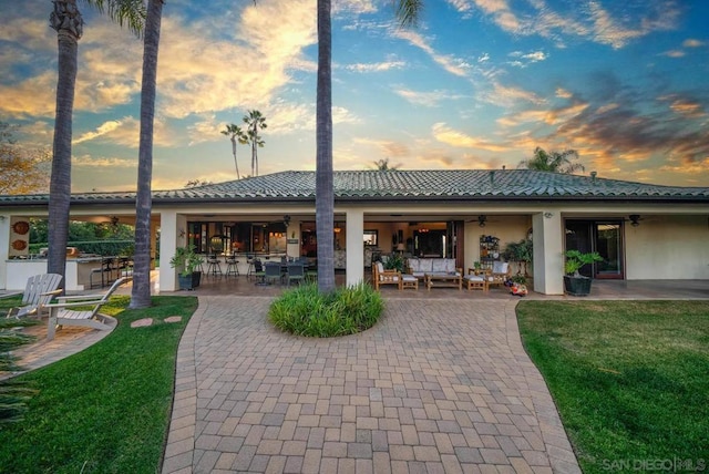 back house at dusk with ceiling fan, a yard, and a patio