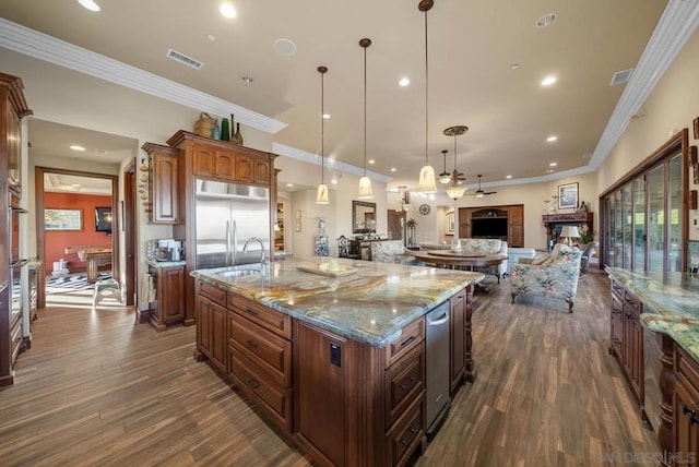 kitchen featuring stainless steel built in refrigerator, a spacious island, sink, decorative light fixtures, and a multi sided fireplace