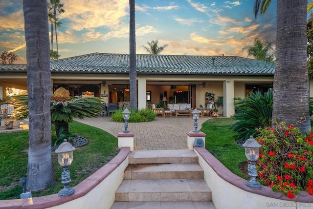 back house at dusk featuring a lawn, a patio area, and outdoor lounge area