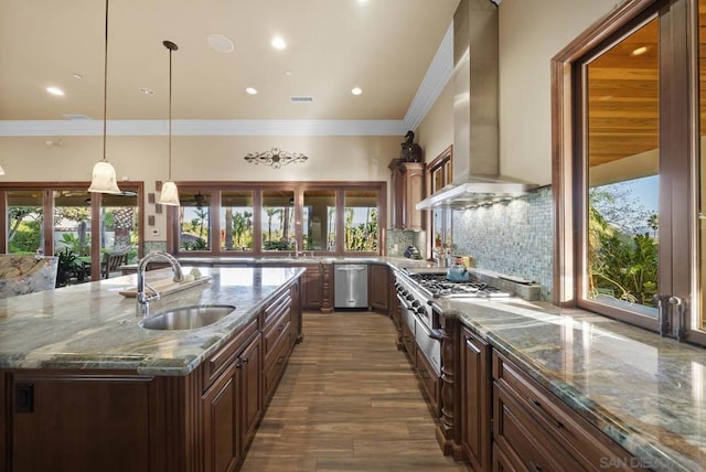 kitchen with a kitchen island with sink, dark stone counters, sink, wall chimney exhaust hood, and decorative light fixtures