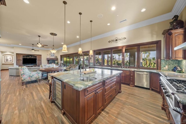 kitchen with appliances with stainless steel finishes, sink, a center island with sink, wine cooler, and hanging light fixtures