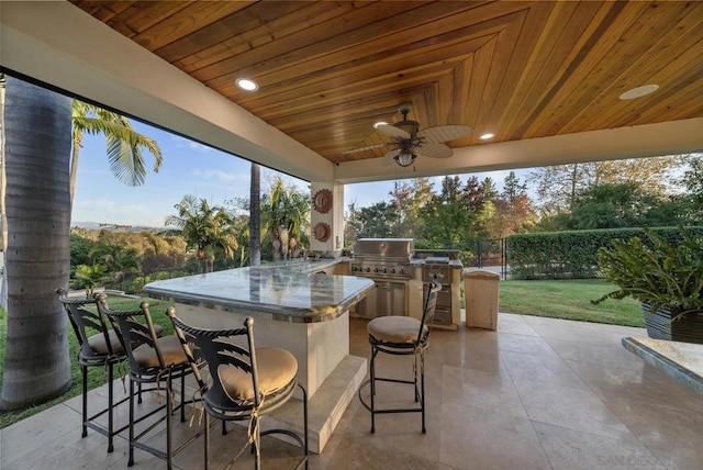 view of patio featuring a bar, an outdoor kitchen, ceiling fan, and a grill