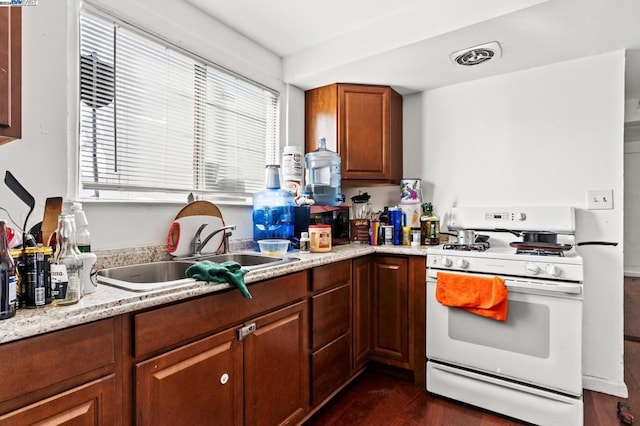 kitchen with light stone counters, sink, dark hardwood / wood-style floors, and white gas range oven