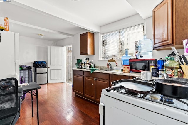 kitchen featuring beam ceiling, sink, dark wood-type flooring, and white appliances