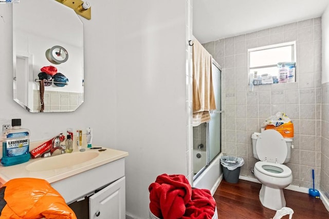 full bathroom featuring combined bath / shower with glass door, wood-type flooring, toilet, vanity, and tile walls