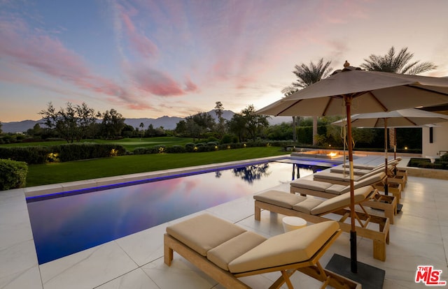 pool at dusk with a mountain view, a yard, and a patio area