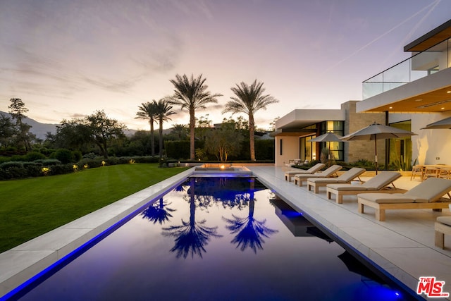 pool at dusk featuring a lawn and a patio area