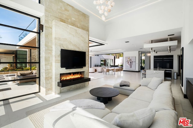 tiled living room with a high end fireplace, a notable chandelier, a high ceiling, and a wealth of natural light