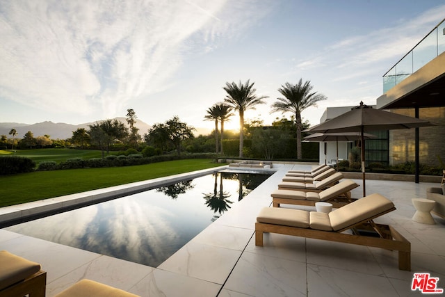 pool at dusk with a lawn, a mountain view, a patio area, and a hot tub