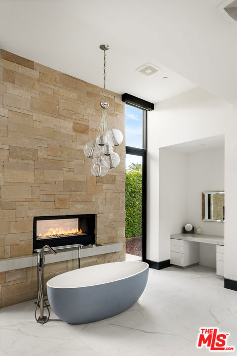 bathroom with a large fireplace, a wall of windows, and a tub to relax in